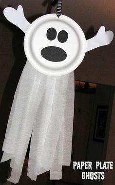 a paper plate ghost hanging from the ceiling with eyes and hands on it's face