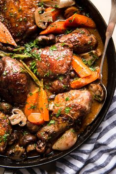 a skillet filled with chicken and carrots on top of a table next to a striped towel