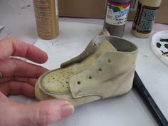 a person is holding an old shoe with holes in the bottom and inside, on a table next to paint cans