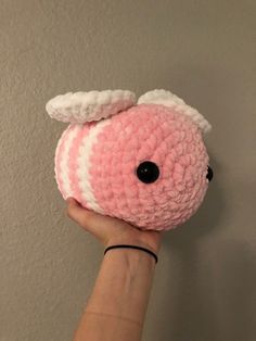 a hand holding a pink and white crocheted stuffed animal with black eyeballs