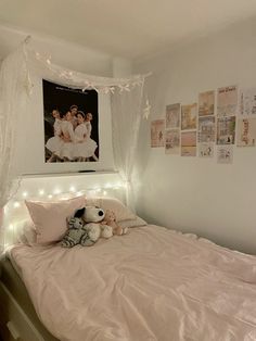 a white bed with pink sheets and lights on the headboard is decorated with pictures