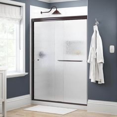 a bathroom with blue walls and white towels hanging on the shower door, next to a window