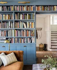 a living room filled with lots of books on top of a blue book shelf next to a stair case