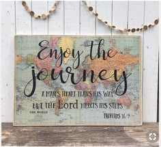 a wooden sign that says enjoy the journey and is hanging on a white wall with string lights