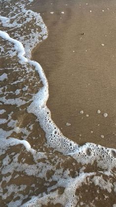 an ocean wave rolls in on the sand at the edge of the beach with white foam