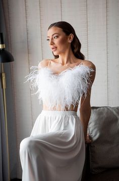 a woman sitting on a couch wearing a white dress with feather bolery around her shoulders