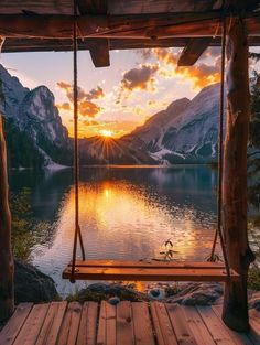 a wooden porch with a swing hanging from it's side overlooking a lake and mountains