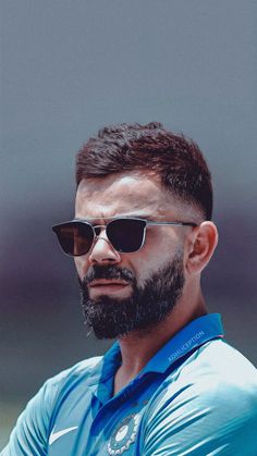 a man with sunglasses and a beard wearing a blue shirt is looking off to the side