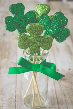 four leaf clovers in a glass vase with green bow on the side and glittered top