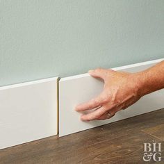 a hand is reaching for the edge of a white tile strip on a wood floor