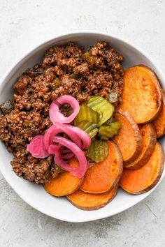 a bowl filled with meat and vegetables on top of a white countertop next to sliced onions