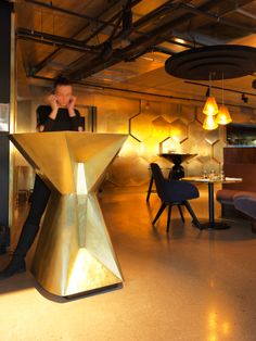 a man sitting at a table in a room with chairs and lights hanging from the ceiling