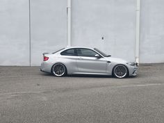 a silver car is parked in front of a white wall and grey concrete parking lot