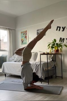 a woman doing a handstand on a yoga mat in a bedroom with a bed