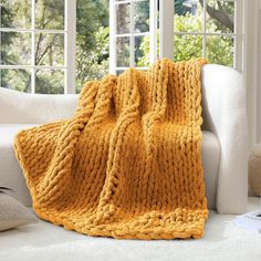 a yellow knitted blanket sitting on top of a white couch next to a window