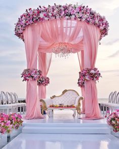 an outdoor wedding setup with pink drapes, flowers and chandelier on the beach