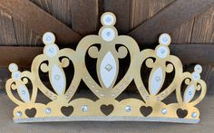 a gold tiara with hearts and jewels on the front, hanging from a wooden wall