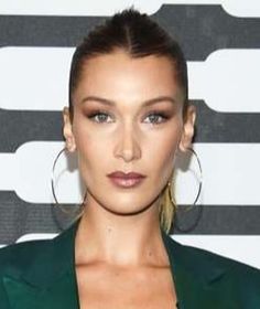 a woman wearing large hoop earrings and a green blazer is posing for the camera