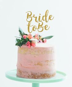 a pink cake with gold lettering that says bride to be sitting on top of it