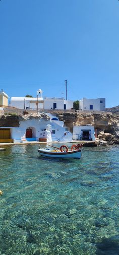 two boats in the clear blue water near a white building and some buildings with red doors