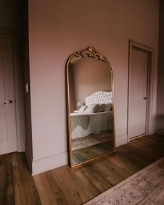 a large gold mirror sitting on top of a wooden floor next to a white bed