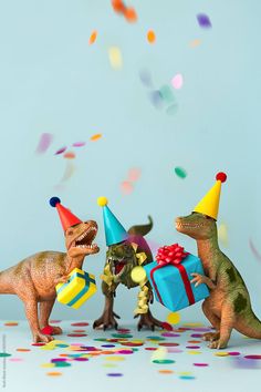 three toy dinosaurs with party hats and confetti