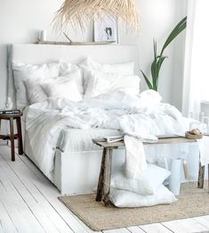 a bed with white linens and pillows in a room next to a plant on the floor