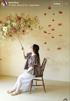 a woman sitting on a chair holding a bunch of flowers in her hand and looking up at the sky