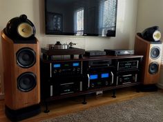 an entertainment center with stereo, speakers and a large television mounted on the wall behind it