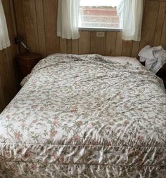 a bed in a room with wood paneling and white curtains on the windowsill