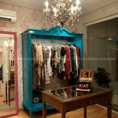 a blue armoire with clothes on hangers and a chandelier hanging from the ceiling