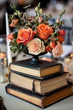 an arrangement of flowers in a vase on top of two books at a wedding reception