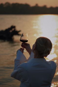 a woman holding a glass of wine while standing in front of a body of water