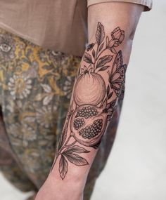 a person with a tattoo on their arm holding onto a piece of fruit and leaves