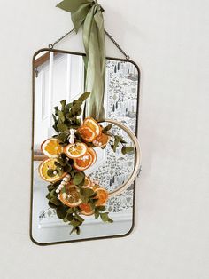 a mirror hanging on the wall with oranges and leaves attached to it's frame