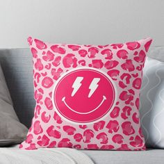 a pink leopard print pillow sitting on top of a couch with a smiley face in the middle