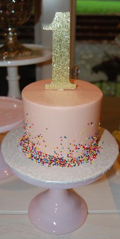 a pink cake with sprinkles and a number one on top is sitting on a table