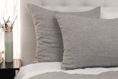 two gray pillows sitting on top of a bed next to a night stand with flowers