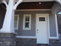 a white door and window on a gray house with stone pillars in front of it