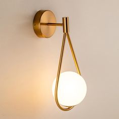 a wall light with a white ball hanging from it's side and a gold metal arm