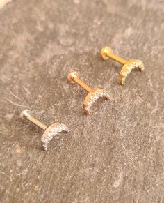 two pairs of gold and diamond studs sitting on top of a stone slab,