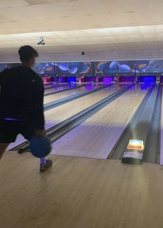 a man standing next to a bowling alley holding a blue ball