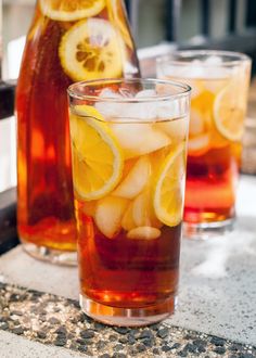 two glasses filled with ice and lemon slices next to a pitcher of water on a table