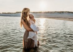 a woman holding a baby in her arms while standing in the water near the beach