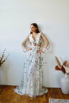 a woman standing in front of a white wall wearing a dress with flowers on it