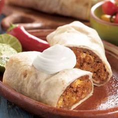 two burritos on a plate with sour cream in the middle and salsa around them