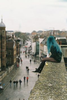 a woman sitting on top of a building next to a wet street filled with people