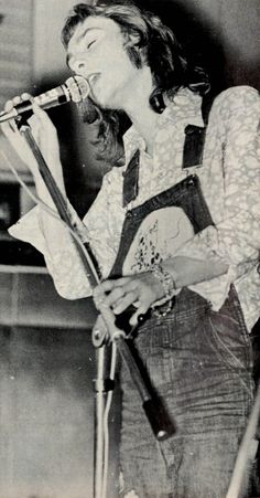 a woman singing into a microphone while holding a guitar in her right hand and wearing overalls