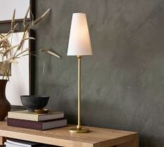 a wooden table with a lamp and books on it in front of a gray wall