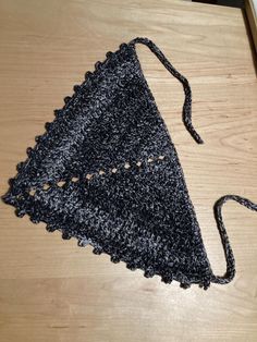 a crocheted triangle on a wooden table with a black string attached to it